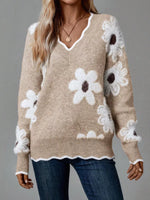 Beige sweater with white floral patterns worn by a person on a gray background