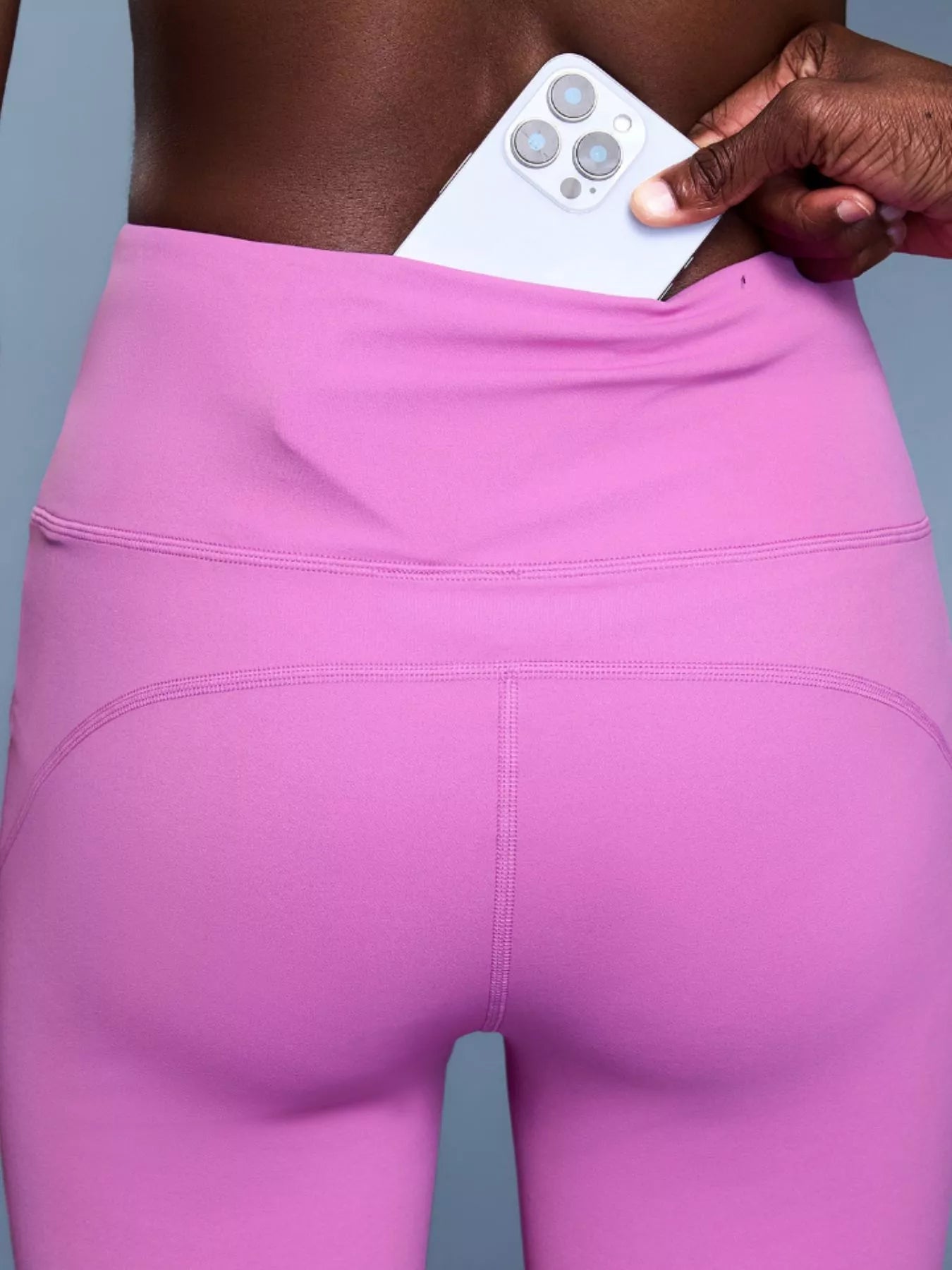Person wearing pink leggings holding a white phone with a gray background