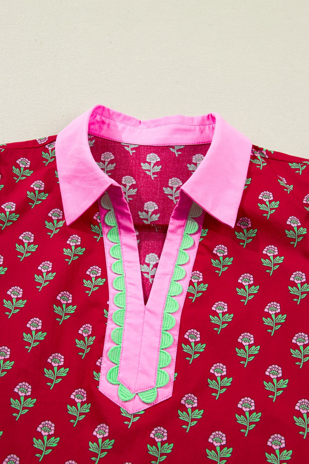 Red shirt with pink collar and green accents on a beige background