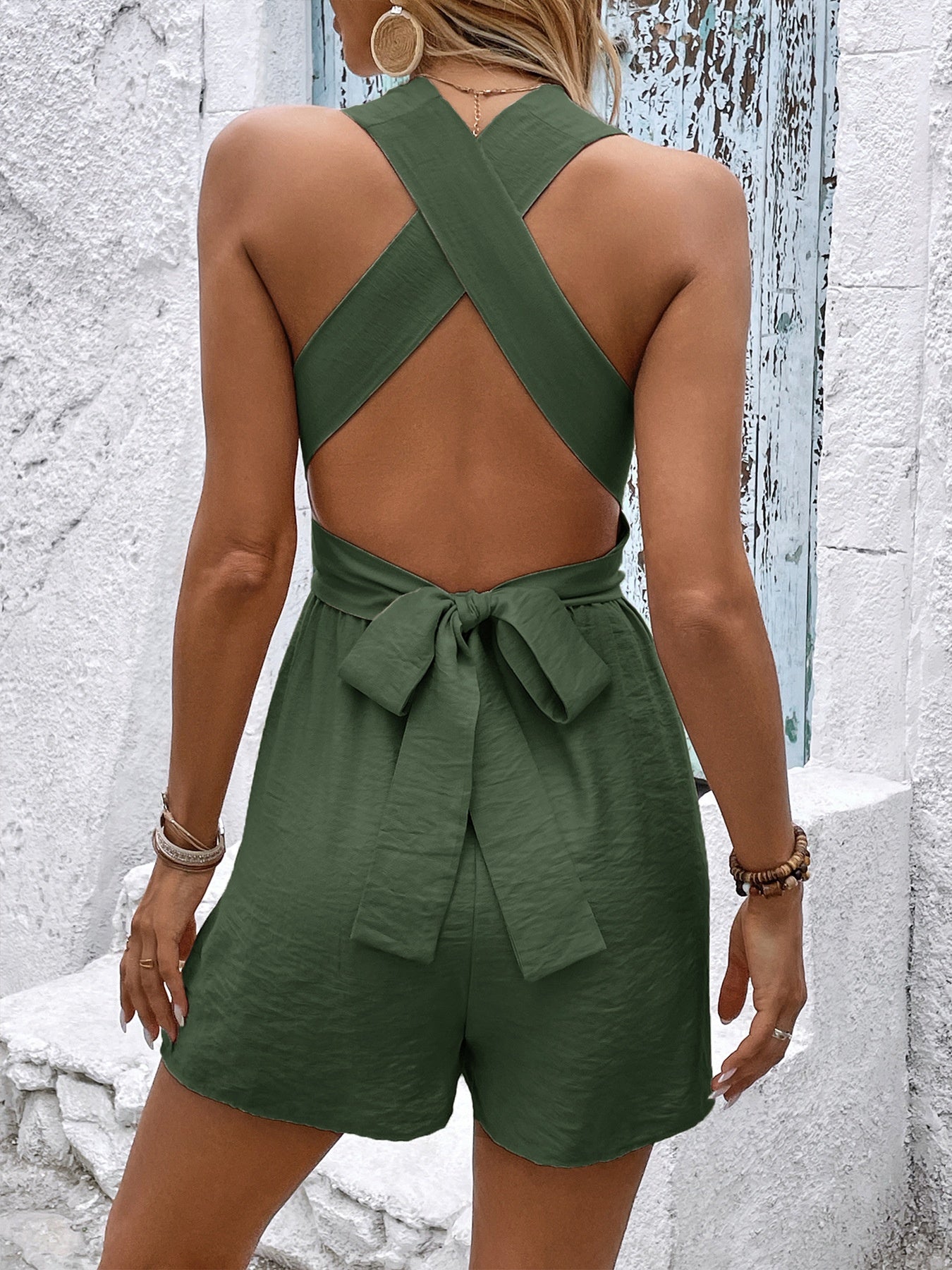 Green romper with open back worn by a person against a textured white wall.