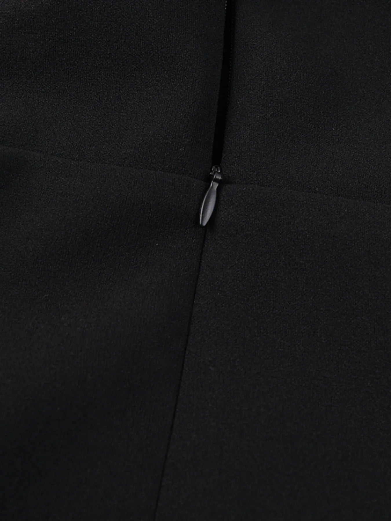 Close-up of a black coat with a zipper detail on a dark background