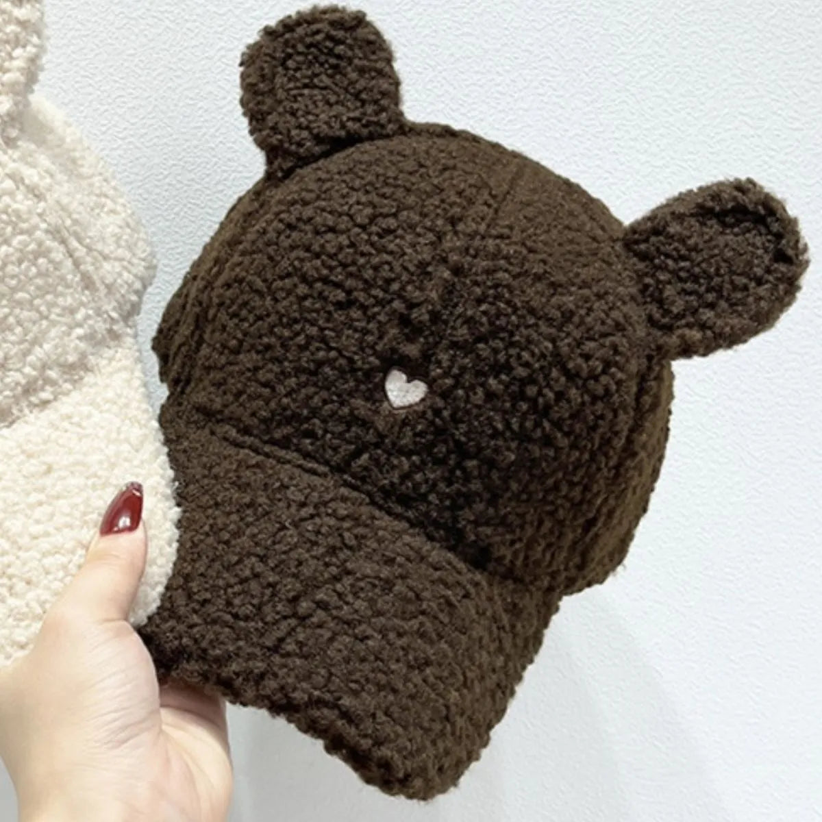 Brown teddy bear hat with ears held by a hand against a light background