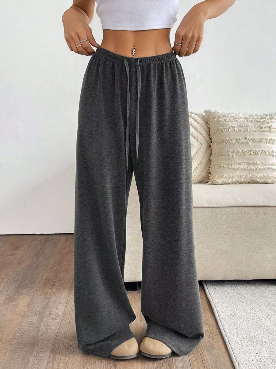 Person wearing dark gray wide-leg pants in a living room setting.