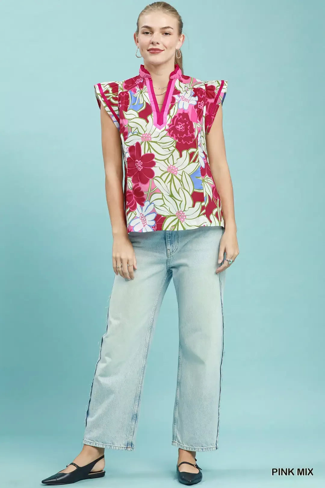 Woman wearing a colorful floral sleeveless top and light blue jeans on a light blue background