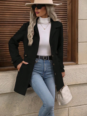 Woman wearing a black coat, white top, blue jeans, and beige hat against a wooden wall.