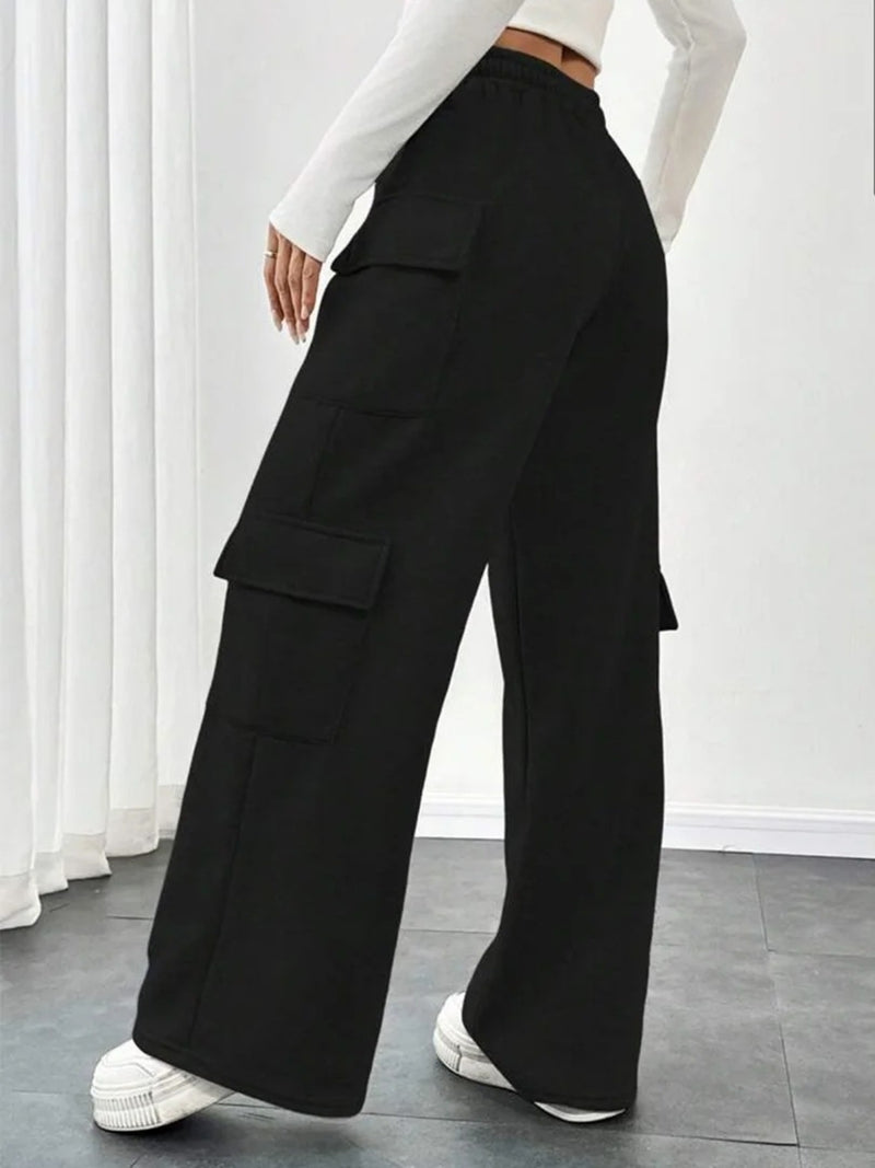 Person wearing black wide-leg pants with cargo pockets in a minimalistic setting.