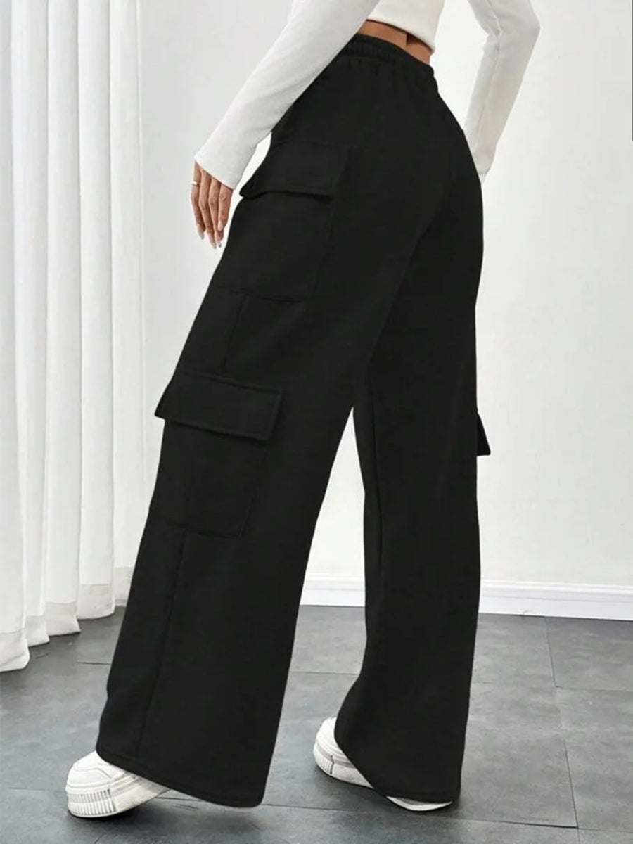 Person wearing black wide-leg pants with cargo pockets in a minimalistic setting.