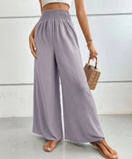 Person wearing light purple wide-leg pants with a white top and brown sandals, holding a straw bag.