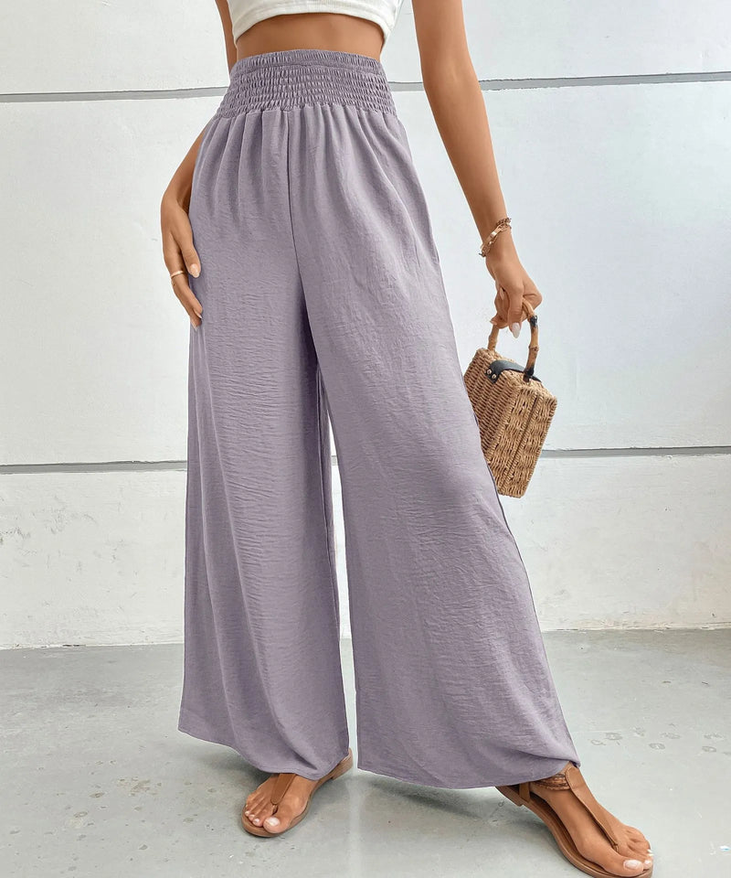 Person wearing light purple wide-leg pants with a white top and brown sandals, holding a straw bag.