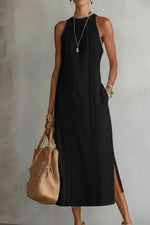 Woman wearing a black sleeveless dress holding a beige handbag against a plain background