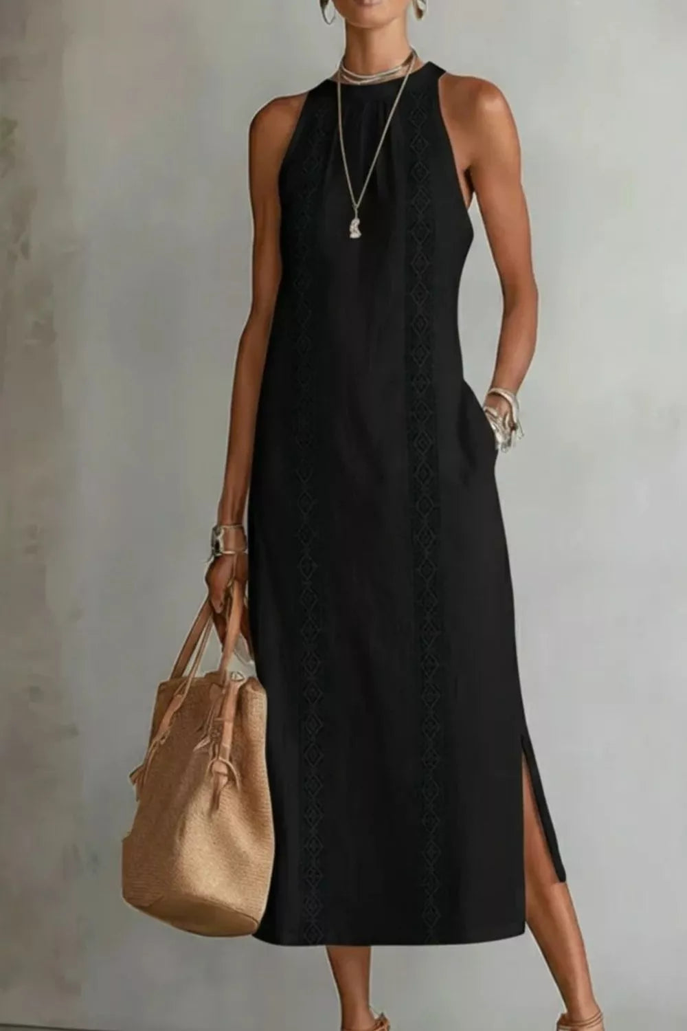 Woman wearing a black sleeveless dress holding a beige handbag against a plain background