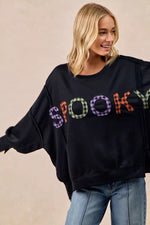 Woman wearing a black sweater with colorful 'SPooky' text on a beige background