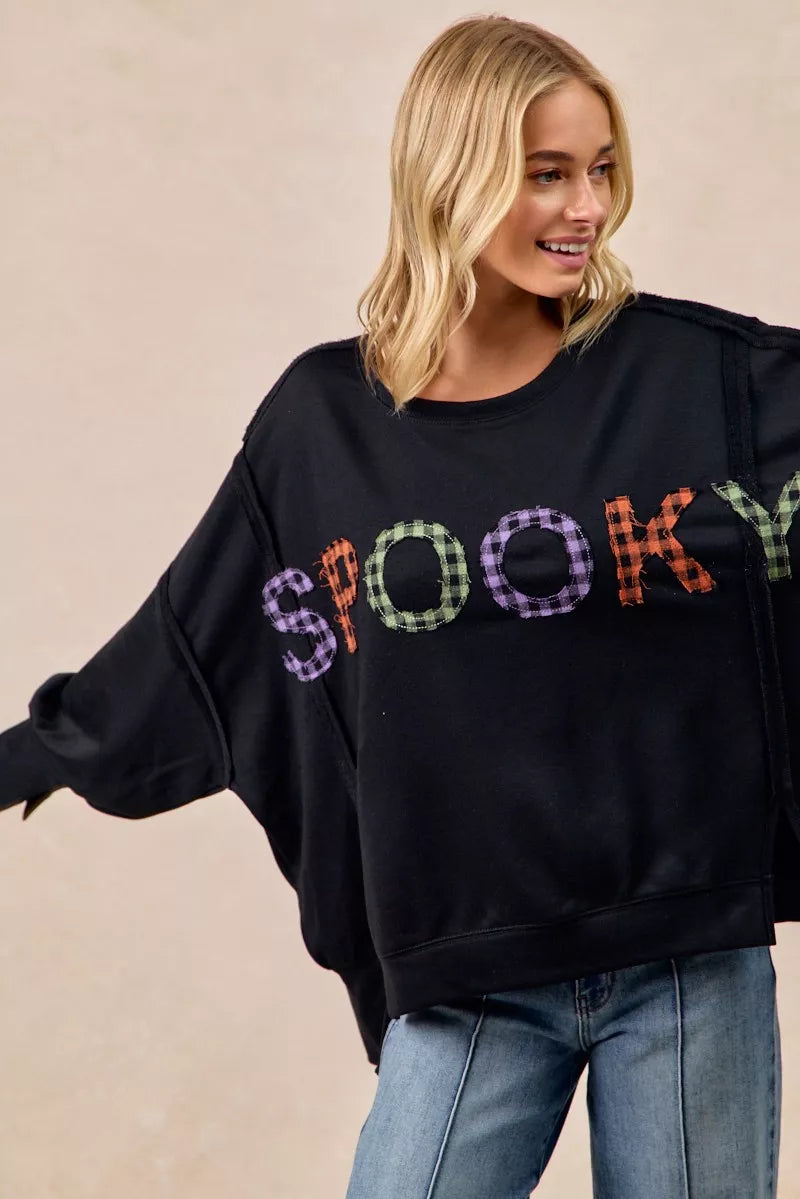 Woman wearing a black sweater with colorful 'SPooky' text on a beige background