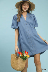 Woman wearing a light blue dress with a straw hat and holding a woven bag with flowers against a light blue background