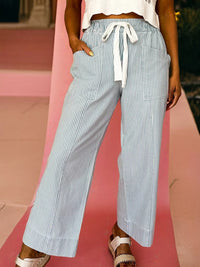Person wearing blue and white striped wide-leg pants on a pink background