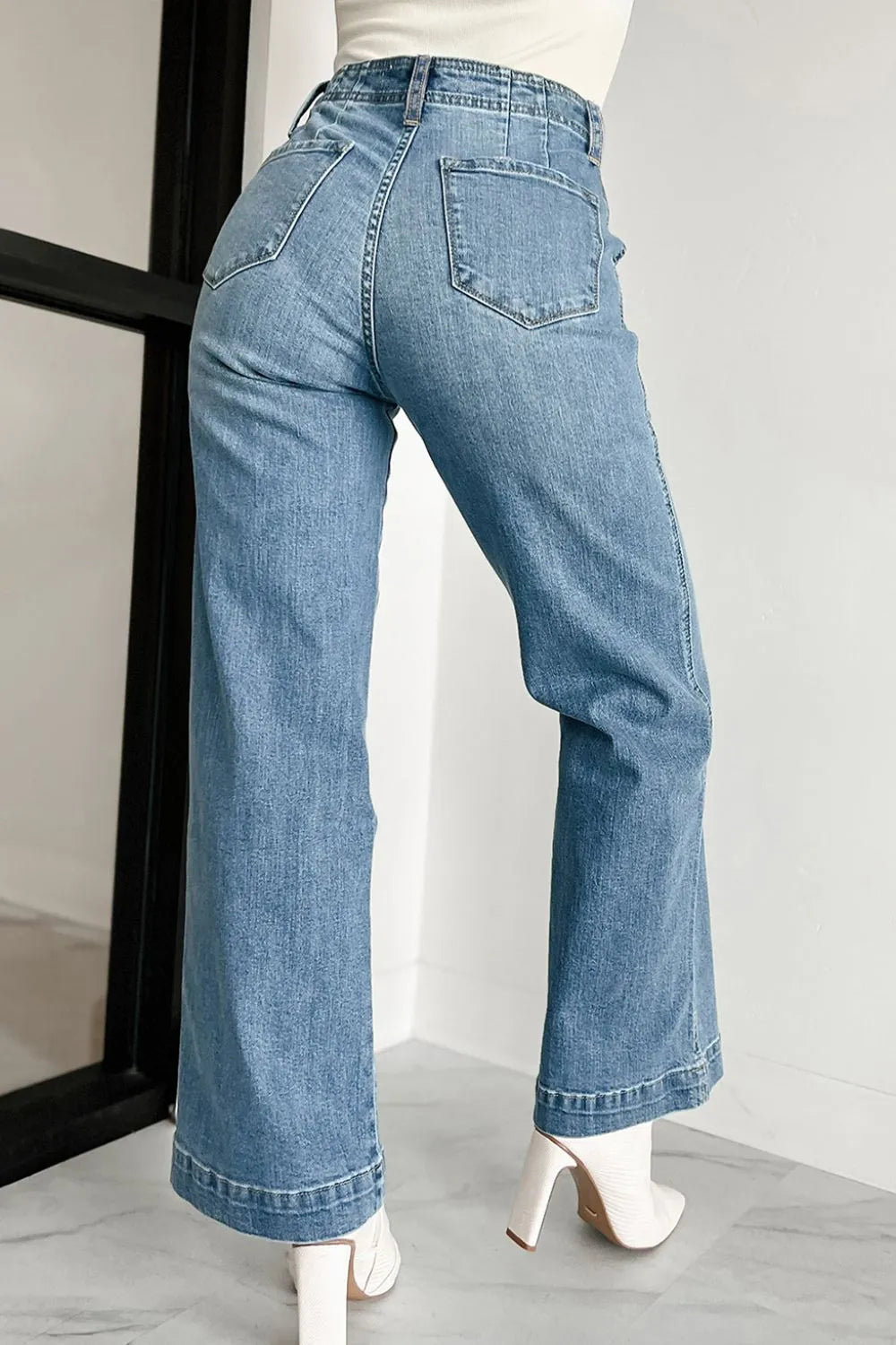 Blue jeans worn by a person on a light gray floor with a white wall background