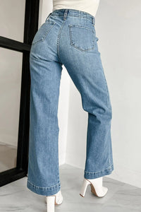 Blue jeans worn by a person on a light gray floor with a white wall background