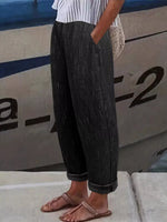 A person wearing dark charcoal gray textured wide-leg trousers with rolled cuffs, paired with a white striped top and flat sandals, standing in front of a boat.