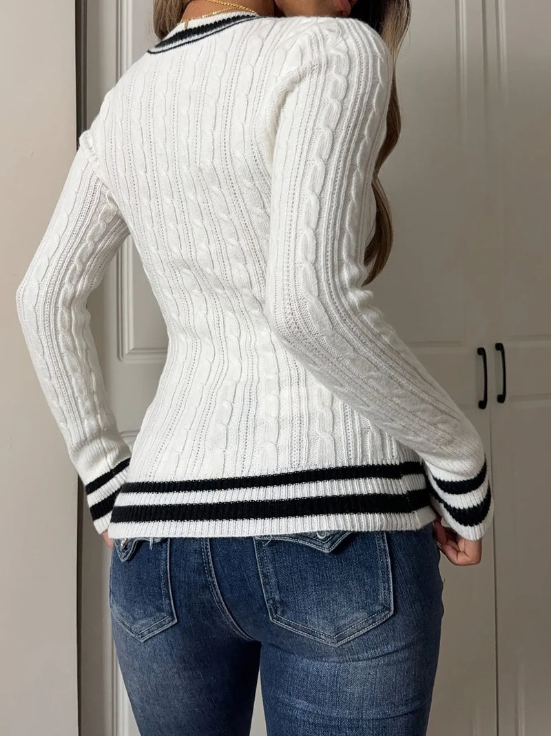 Person wearing a white sweater with black trim in front of a neutral-colored door.
