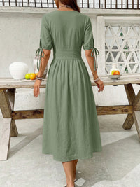 Woman wearing a green dress standing by a wooden table outdoors.