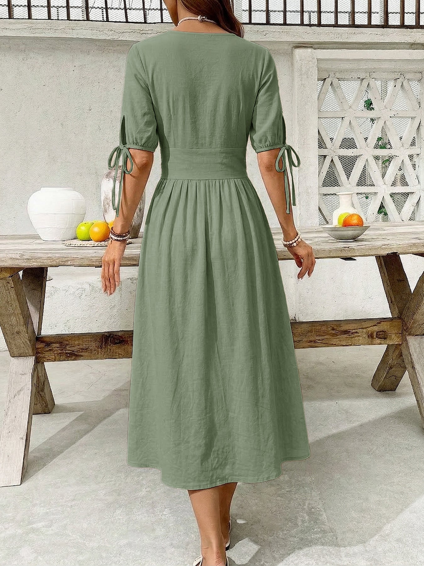 Woman wearing a green dress standing by a wooden table outdoors.