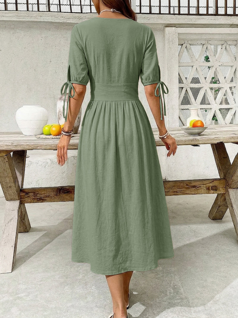 Woman wearing a green dress standing by a wooden table outdoors.