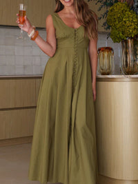 Woman in a long green dress holding a glass of wine in a kitchen setting.