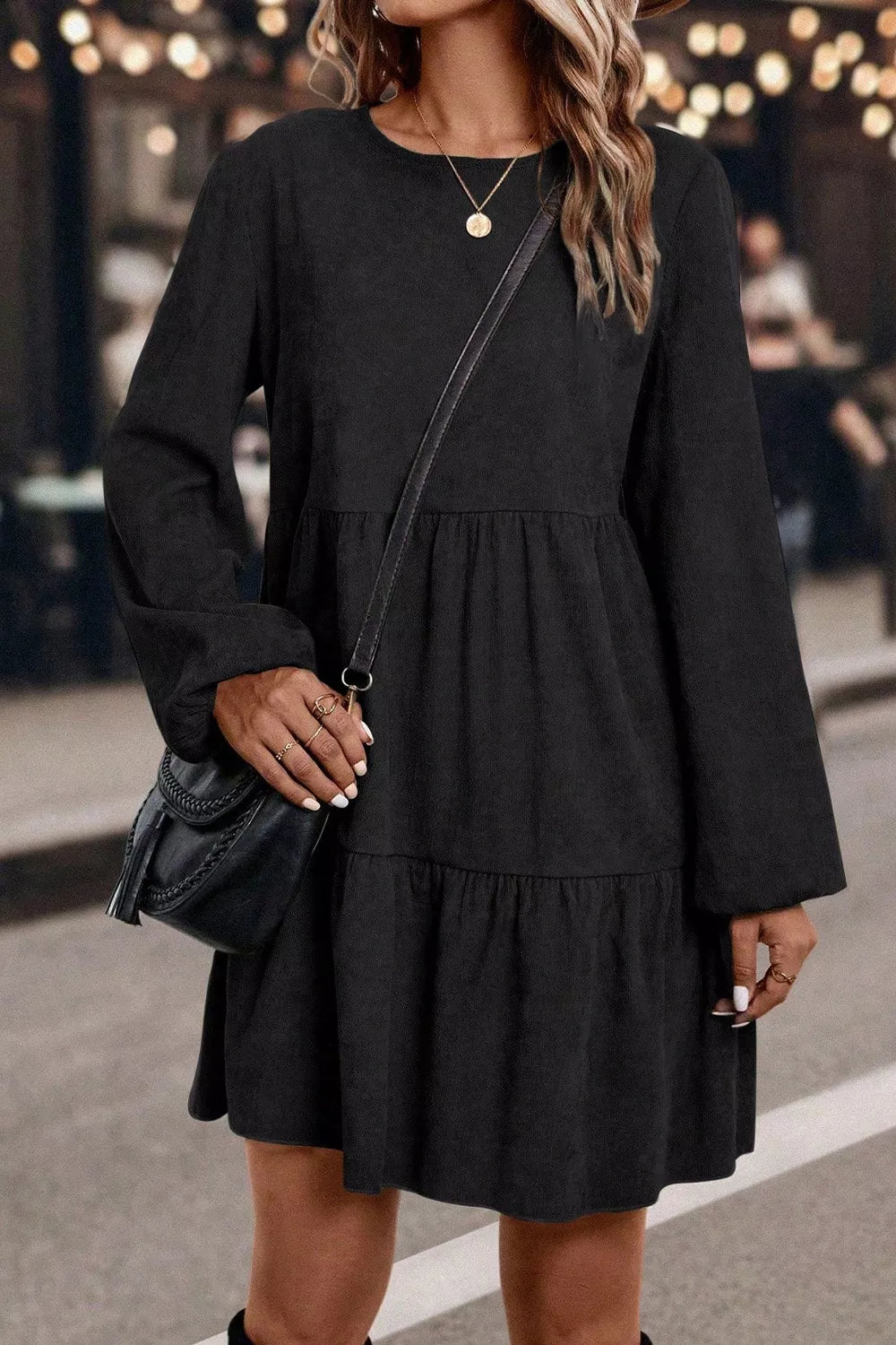 Woman wearing a black dress with long sleeves and a crossbody bag.