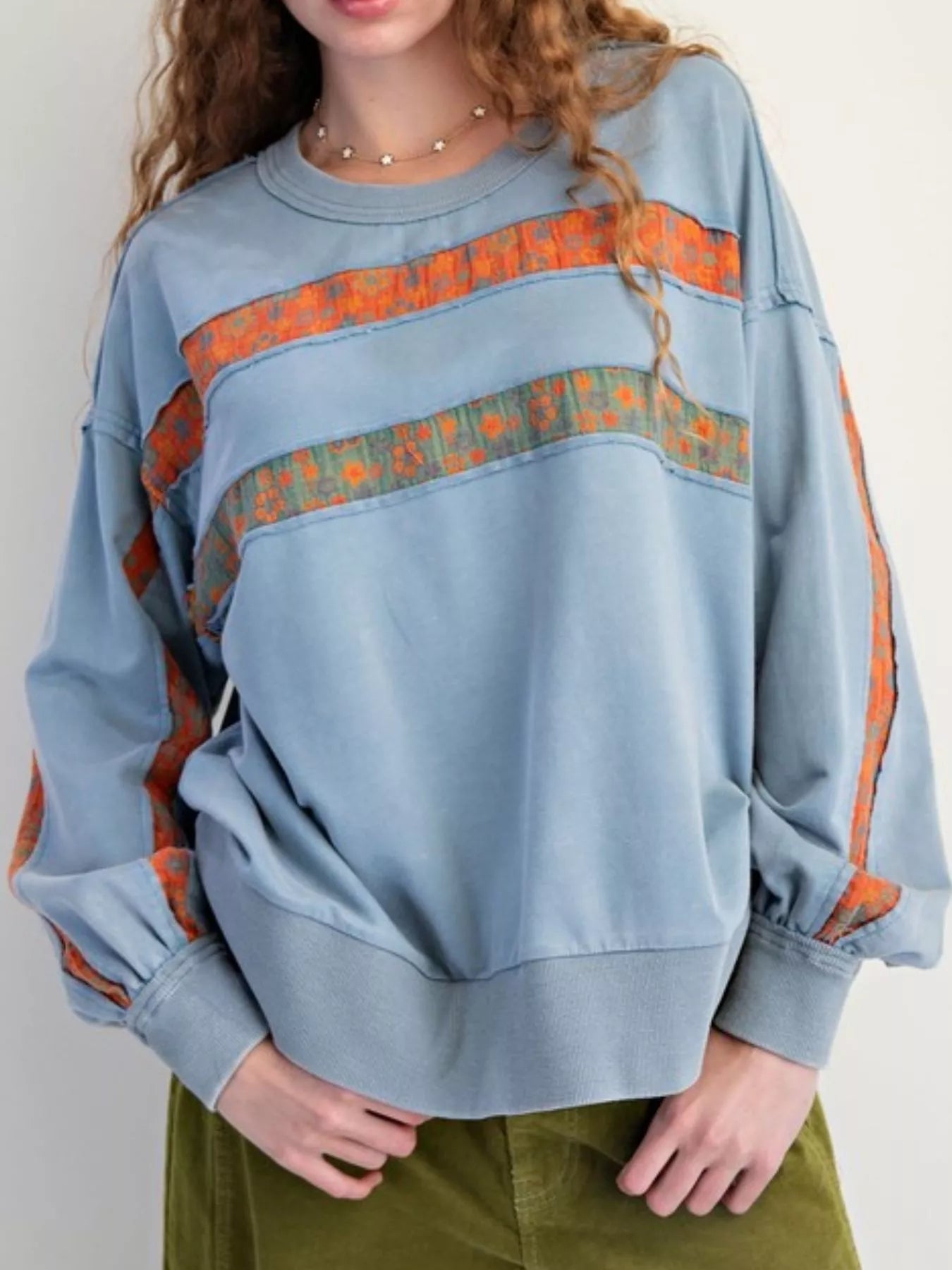 Light blue sweatshirt with orange and green pattern on a plain background