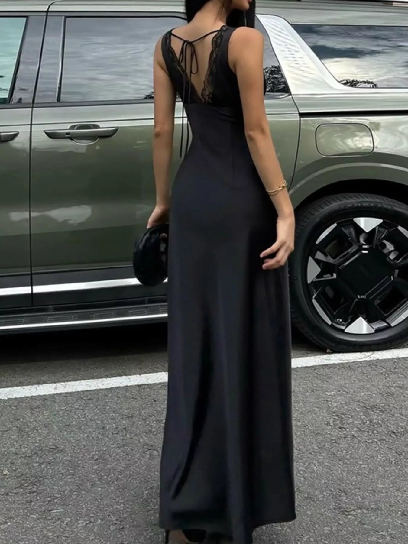 Person wearing a black dress standing next to a green SUV.