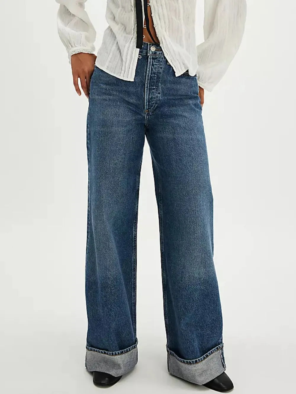 Person wearing blue wide-leg jeans with a white shirt on a light gray background