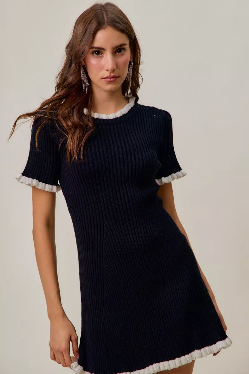 Woman wearing a black dress with white trim on a plain background