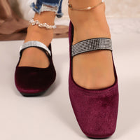 Purple shoes with rhinestone straps worn by a person on a light background
