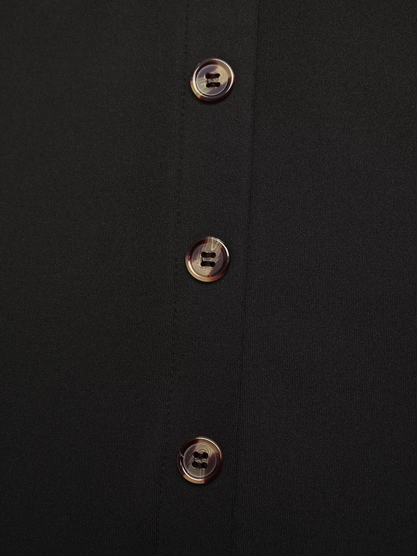 Close-up of a black shirt with gold buttons on a dark background
