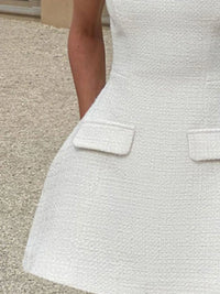 Close-up of a textured white dress with a pocket on a neutral background