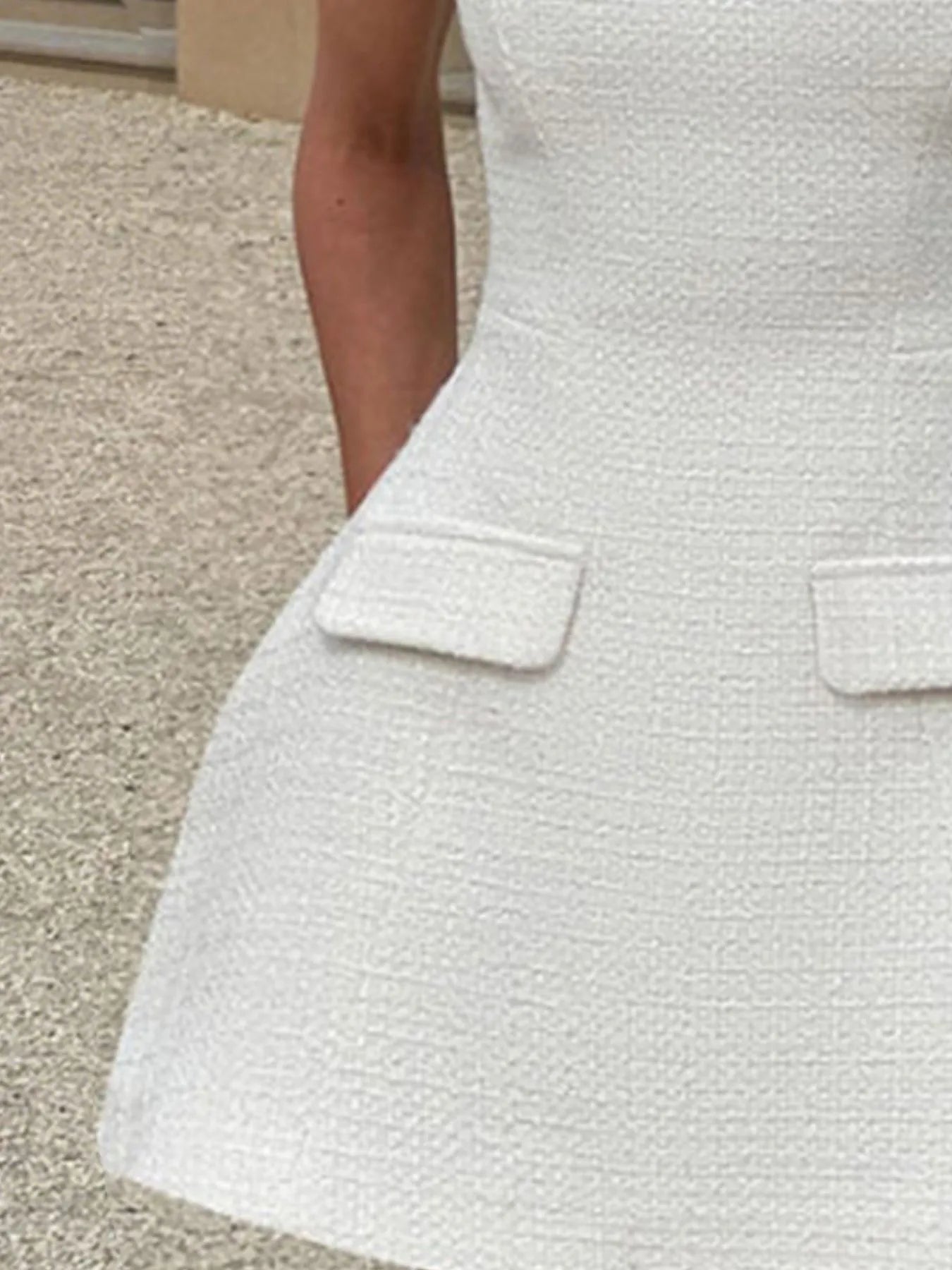 Close-up of a textured white dress with a pocket on a neutral background