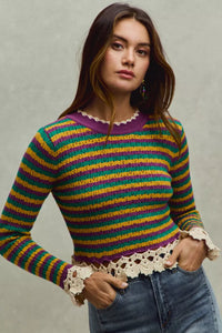 Woman wearing a colorful striped sweater with lace details on a neutral background