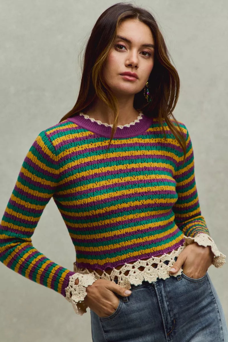 Woman wearing a colorful striped sweater with lace details on a neutral background