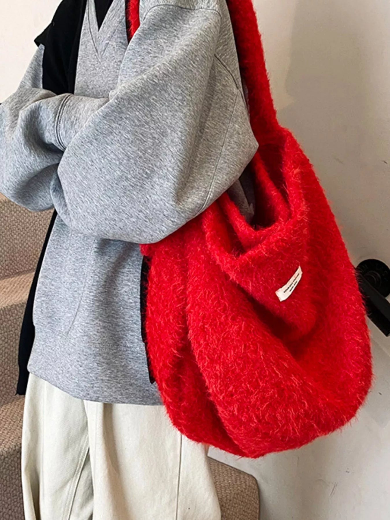 Person wearing a gray sweater and holding a red textured bag.