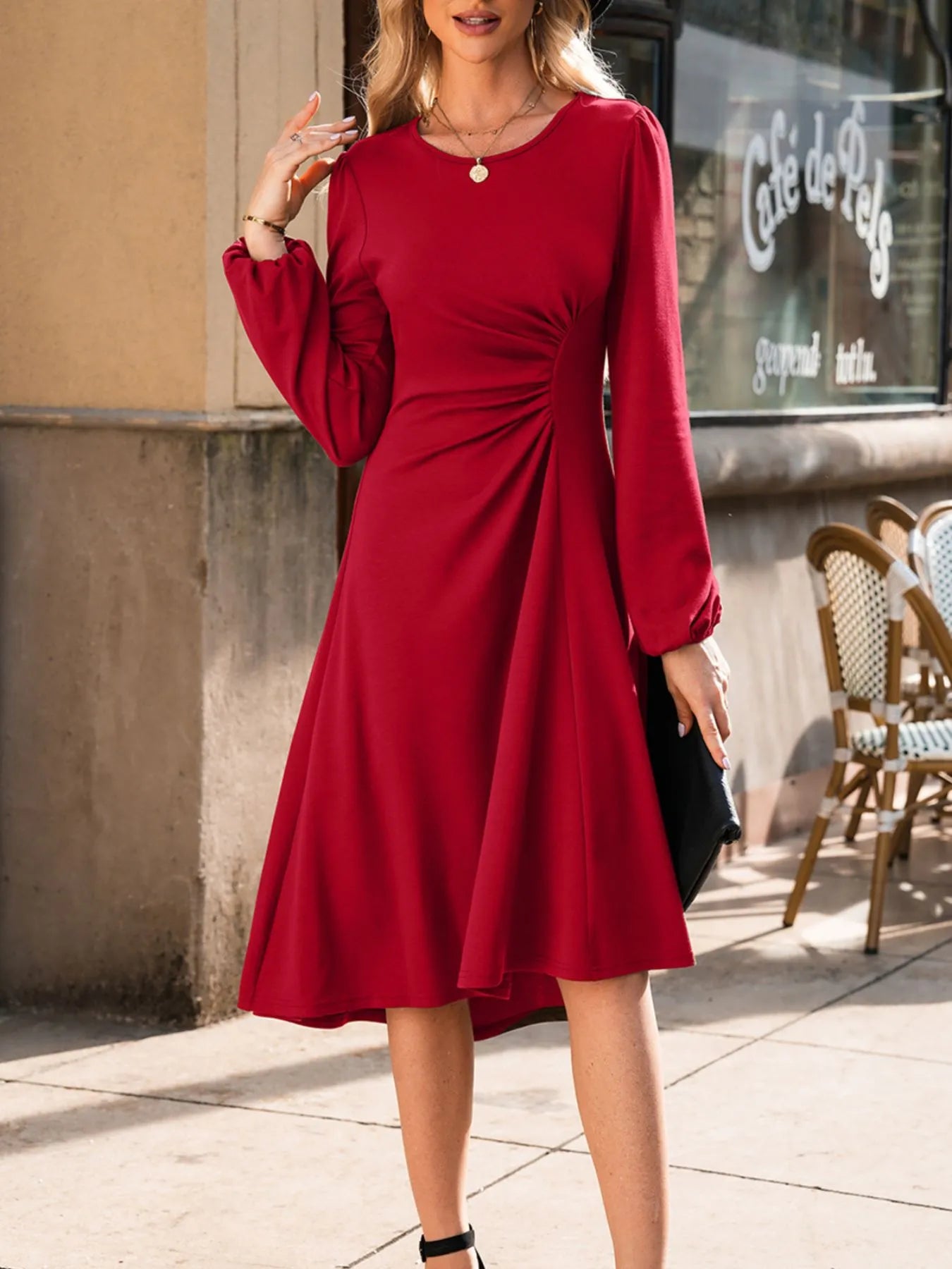 Woman wearing a red dress standing on a sidewalk with a cafe in the background