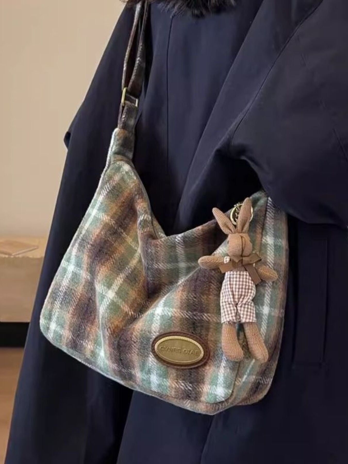 Plaid handbag with a plush rabbit toy attached, held by a person wearing a dark coat.