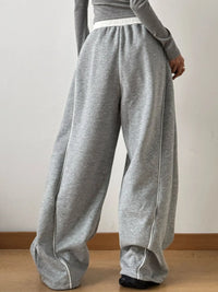 Person wearing gray sweatpants with white trim on a plain background