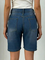 Blue denim shorts worn by a person on a plain background