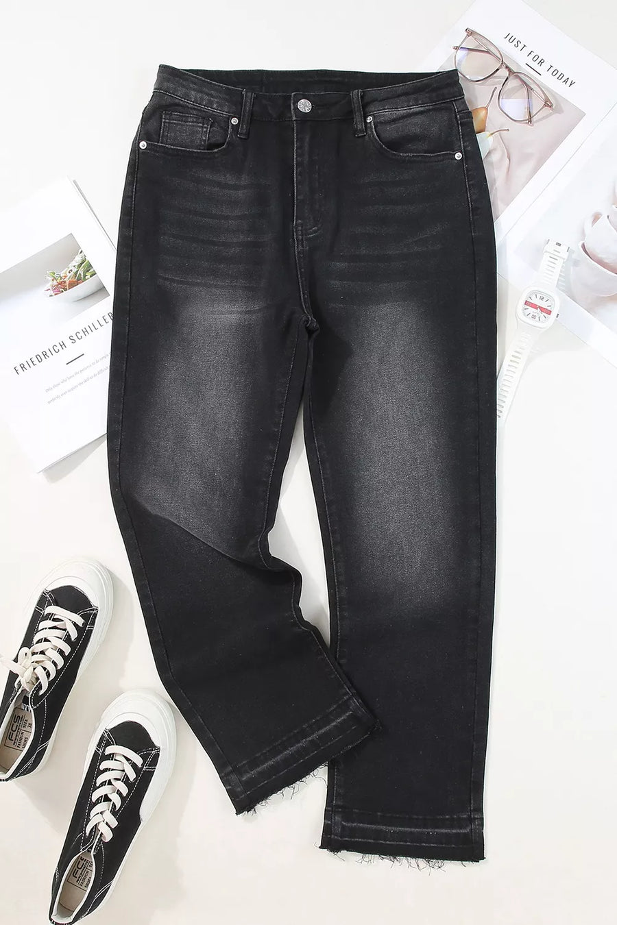 Black jeans on a white surface with sneakers and a newspaper.