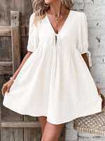 Woman wearing a white dress standing against a rustic wooden and stone wall.