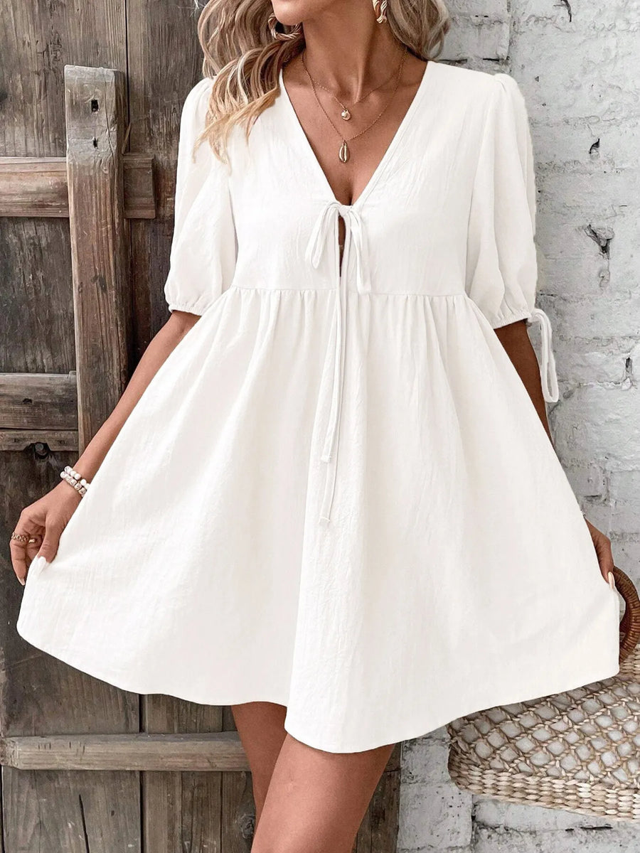 Woman wearing a white dress standing against a rustic wooden and stone wall.