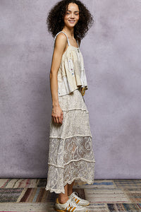 Woman wearing a layered dress with lace details against a textured wall.