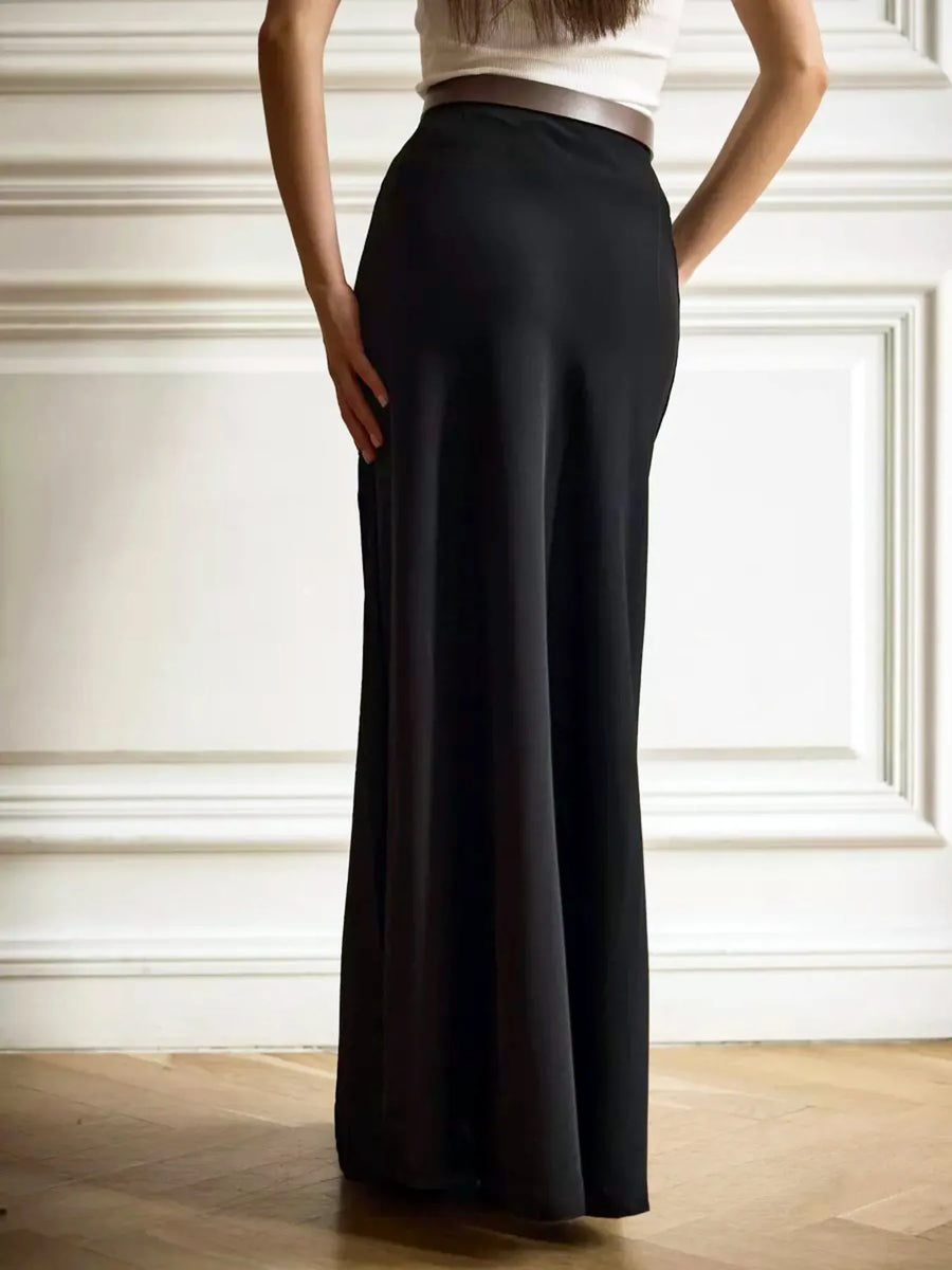 Person wearing black wide-leg pants and a white top against a white wall.