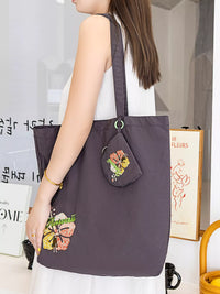 Person holding a dark purple tote bag with floral designs in an indoor setting.