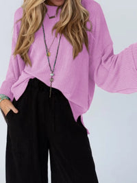 Person wearing a pink sweater and black pants against a white background